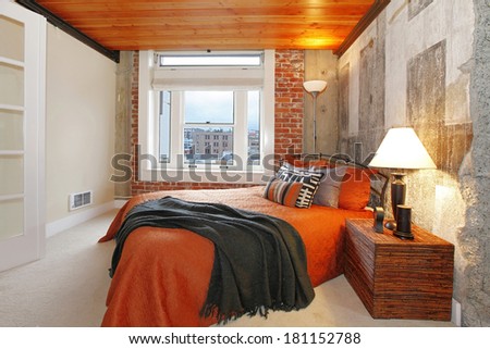 Modern bedroom with brick trim, concrete broken wall and wood plank paneled ceiling. Furnished with iron bed and nightstand.