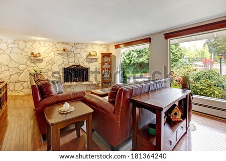 Luxury living room with stone wall trim and fireplace. Furnished with leather couches, antique cabinet with drawers and table.