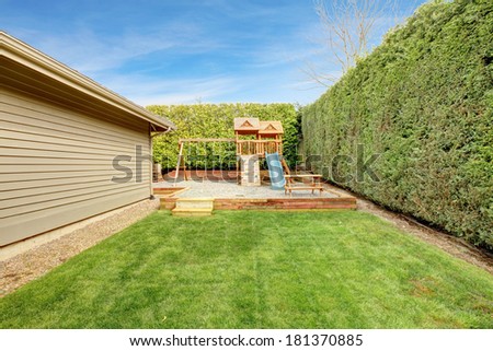 Home play yard for kids with swings, chute and climbing wall. Surrounded by trimmed hedges