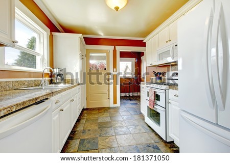 Orange walls kitchen room with concrete floor. Furnished with white storage combination. View of small dining area