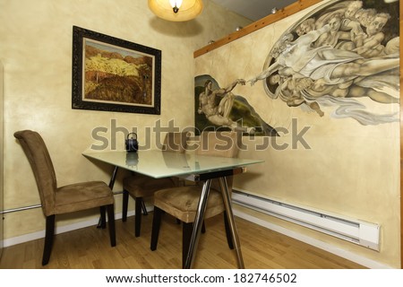 Glass top dining table with chairs. View of beautiful painted wall mural. Michelangelo work  - Creation of Adam.