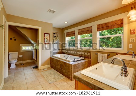 Bathroom with ceramic floor, tile base tub, washbasin cabinet with two sinks and toilet.
