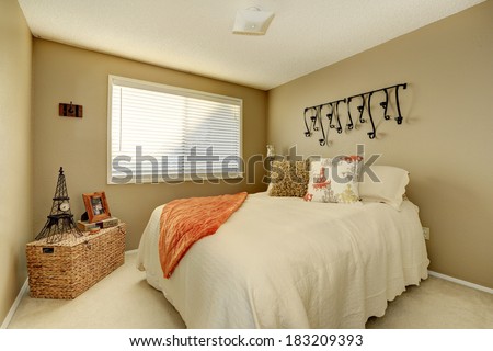 Gentle tones bedroom with ivory bedding, pillows and orange blanket. Room decorated with wicker chest and small eiffel tower