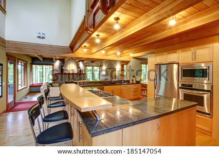 View of kitchen back with black high stools, steel appliances and ceiling beams