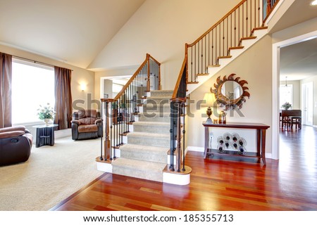View of hardwood hallway with staircase and  living room with leather armchairs and table