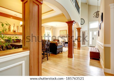 Spacious high ceiling house with wooden column in it. View of hallway with ottoman, living area and entrance door.