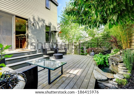 Nice summer backyard with exotic landscape. View of wicker chairs with ottoman and glass top table