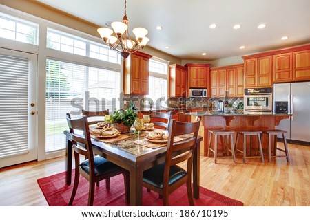 Modern kitchen with steel appliances and island. View of served dining table set on a red rug