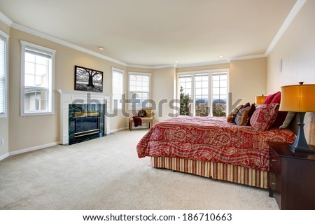 Luxury bedroom with gentle ivory walls, french windows and fireplace. Furnished with bed, nightstand and ottaman
