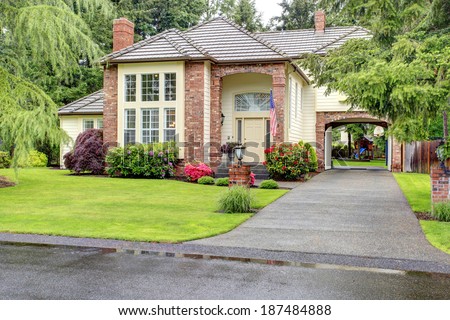 Beautiful curb appeal. Large brick house with siding trim and tile roof. View of entrance high ceiling porch and driveway with arch
