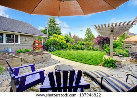 Fenced backyard with lawn, garden bed, shed with woods and pergola. View from patio area with chairs and umbrella