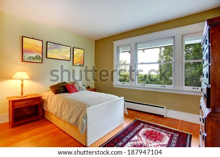 Ivory wall rectangle bedroom with hardwood floor. View of single bed and nightstands. Room has big dresser