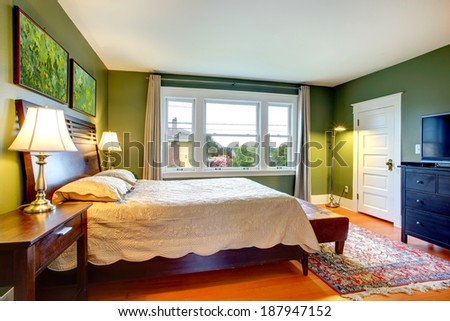 Green walls bedroom with high headboard bed, leather ottoman, black cabinet  and rug