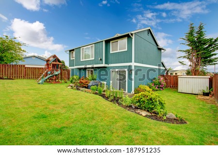 Backyard with green lawn, flower beds and playground for kids