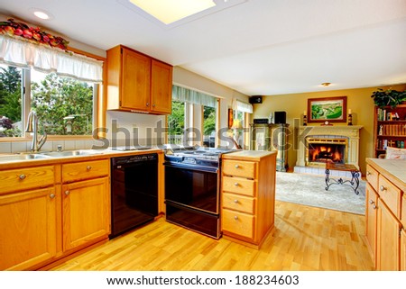 Kitchen room with wooden cabinets and black appliances. View of living room with a fireplace