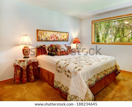Bright bedroom with brown carpet floor. Furnished with bed, covered round table and cabinet