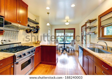 Practical kitchen room interior. View of cabinets, steel appliances, hanging pot rack. Kitchen room has a small dining area