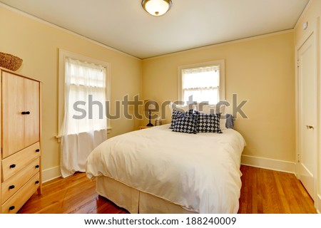Small cozy bedroom with bed and wooden dresser. Room has two windows and hardwood floor