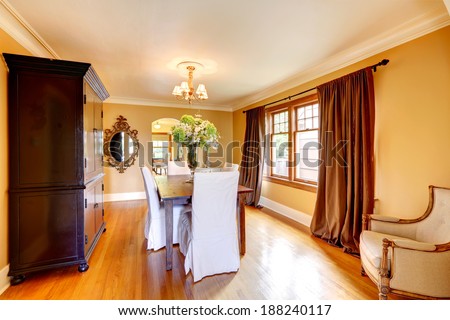 Elegant dining room with wooden table, chairs with white covers and old storage cabinet