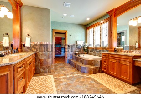 Luxury bathroom with tile wall trim and tile floor. View of vanity with mirror and bath tub with step