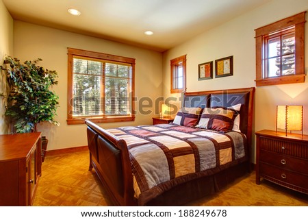 Bedroom with leather headboard bed covered with pleated bedding. Room decorated with fake tree in the corner