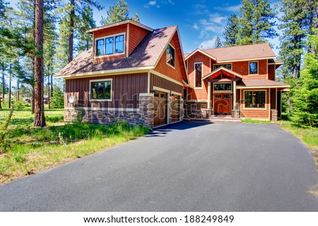 Big luxury house with brown and orange siding trim. View of entrance porch and two car garage