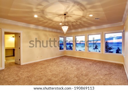 Empty room with ivory walls and brown carpet floor. Beautiful sunset view through the window