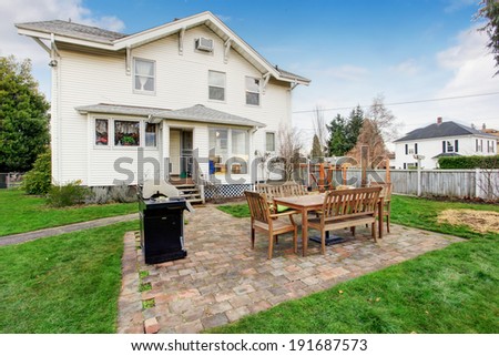 Fenced backyard with small patio area. View of wooden table set and barbecue