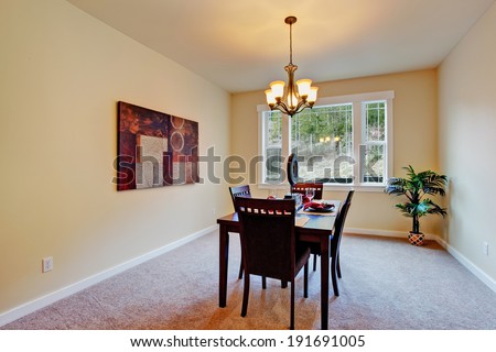Simple and bright dining room with served table. Decorated with wall picture and fake palm tree