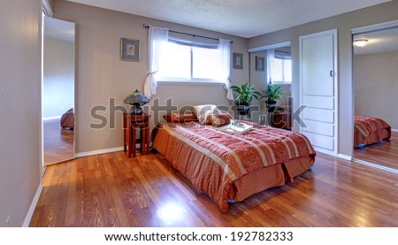 Simple yet comfortable bedroom with mirror doors closets, hardwood floor and small window