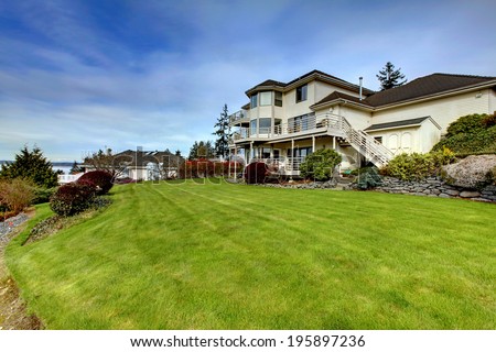 Luxury house  with three level deck. View of well designed backyard with green lawn and bushes.