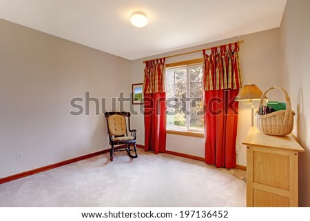 Empty room with window treated with red curtains. Room has just rocking chair, lamp and dresser