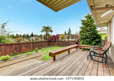 Wooden deck with benches and chair. View of fenced backyard with lawn and flower bed