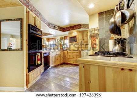 Rustic kitchen with gold wooden cabinets, black appliances and tile floor
