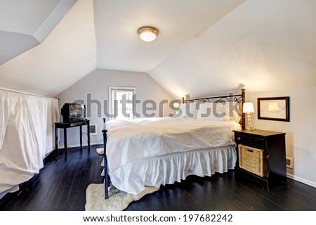 White velux bedroom with vaulted ceiling and old black hardwood floor. Furnished with iron frame bed, nightstand and tv