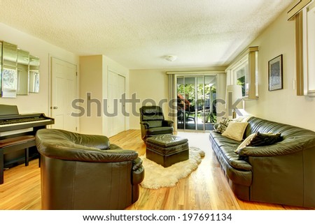 Modern living room with black leather furniture set, piano and ottoman standing on white soft rug. View of walkout deck