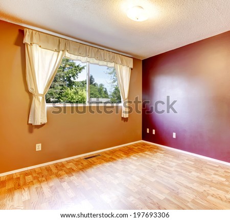 Empty room with burgundy and brown walls, hardwood floor. View of window with soft ivory curtains