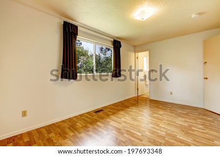 Empty room in soft colors, shiny hardwood floor. View of window with brown curtains