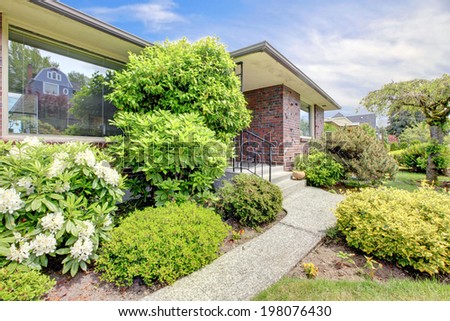 House exterior. Brick house with entrance porch and walkway. View of landscape with blooming bushes