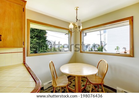 Dining corner in kitchen room with two wide windows. View of rustic round dining table with chairs