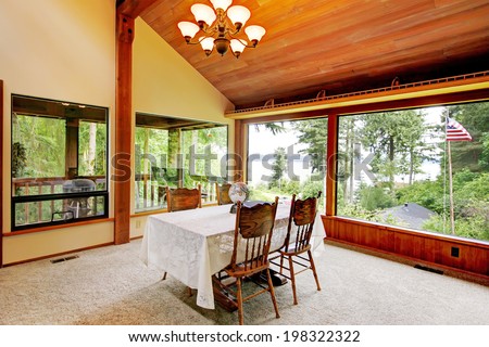 Spacious dining area in log cabin house with high vaulted ceiling and wide window. View of rustic dining table set.