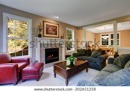 Cozy living room with fireplace, dark green sofas and red leather armchair. View of antique coffee table with drawers