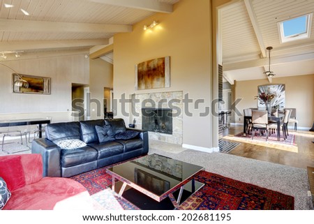 Open floor plan in big luxury house. View of spacious living room with fireplace, black leather couch and coffee table