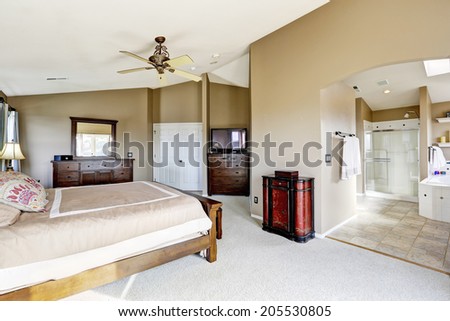 Luxury bright master bedroom interior with bathroom. View of bed with bedroom vanity cabinet, tv and dresser