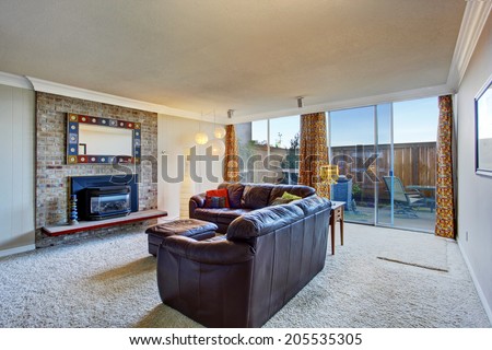 Living room interior with brick background fireplace and leather furniture set. View of slide door to backyard