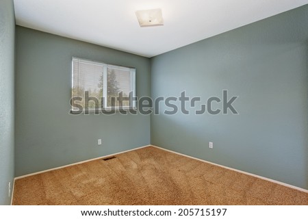 Small empty room in aqua color with one window and soft brown carpet floor