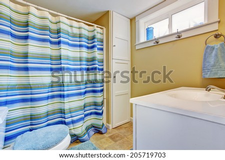 Ivory bathroom with built-in cabinet. Decorated with stripped blue curtain, toilet seat lid cover and rug