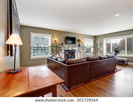 Living room interior with hardwood floor. View of burgundy leather couch and cozy fireplace with tv above it