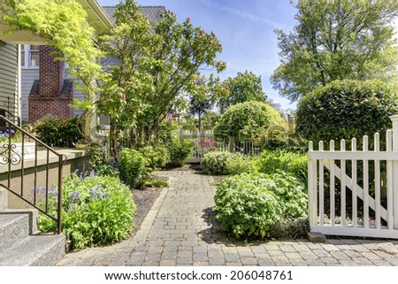 Fenced front yard with open gate. View of walkway and flower beds alongside