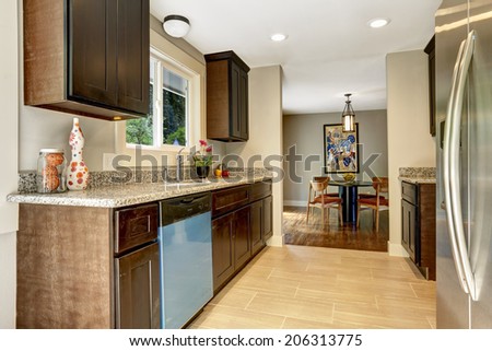 Modern kitchen interior with dark brown storage cabinets with granite counter tops and new tile floor. View of dining area